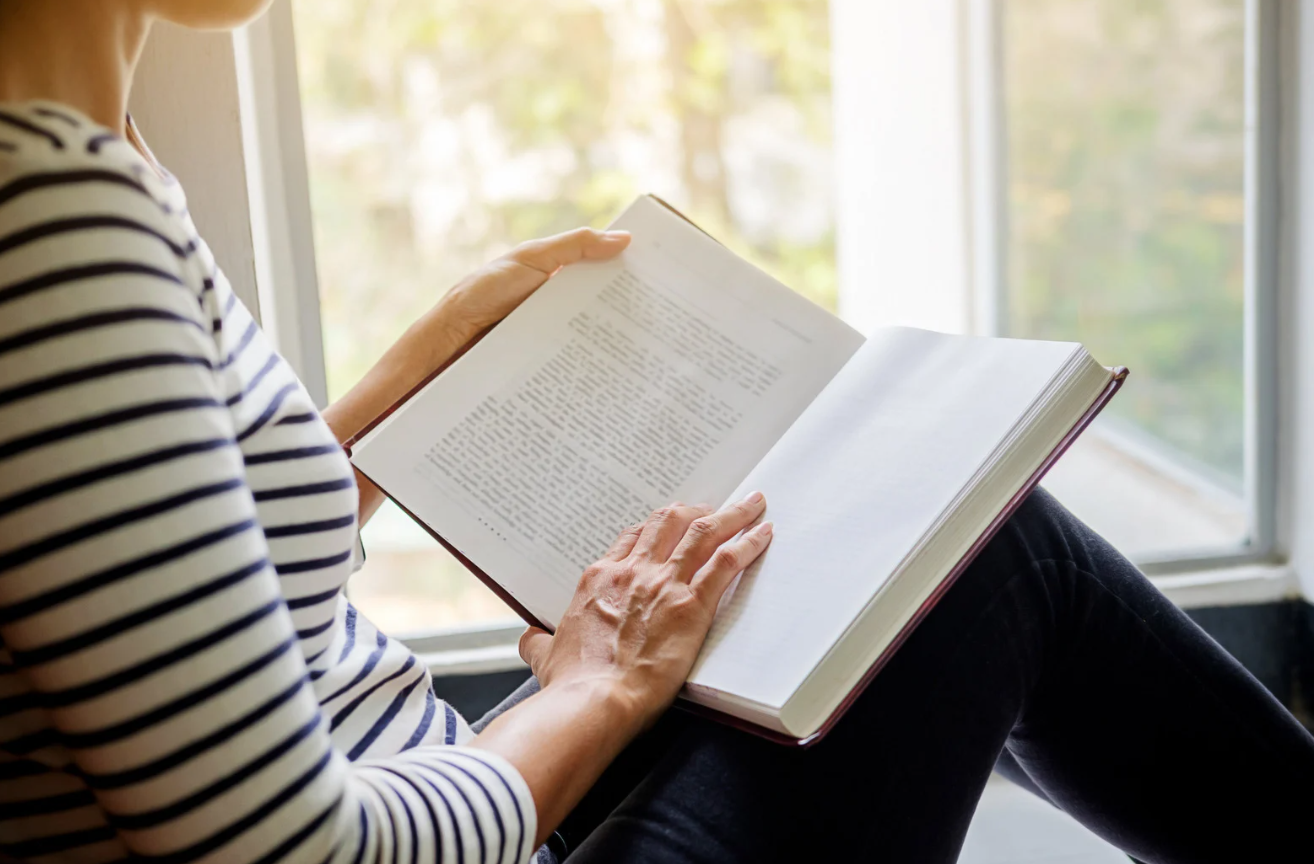 Lady reading a book in a cosy book nook.